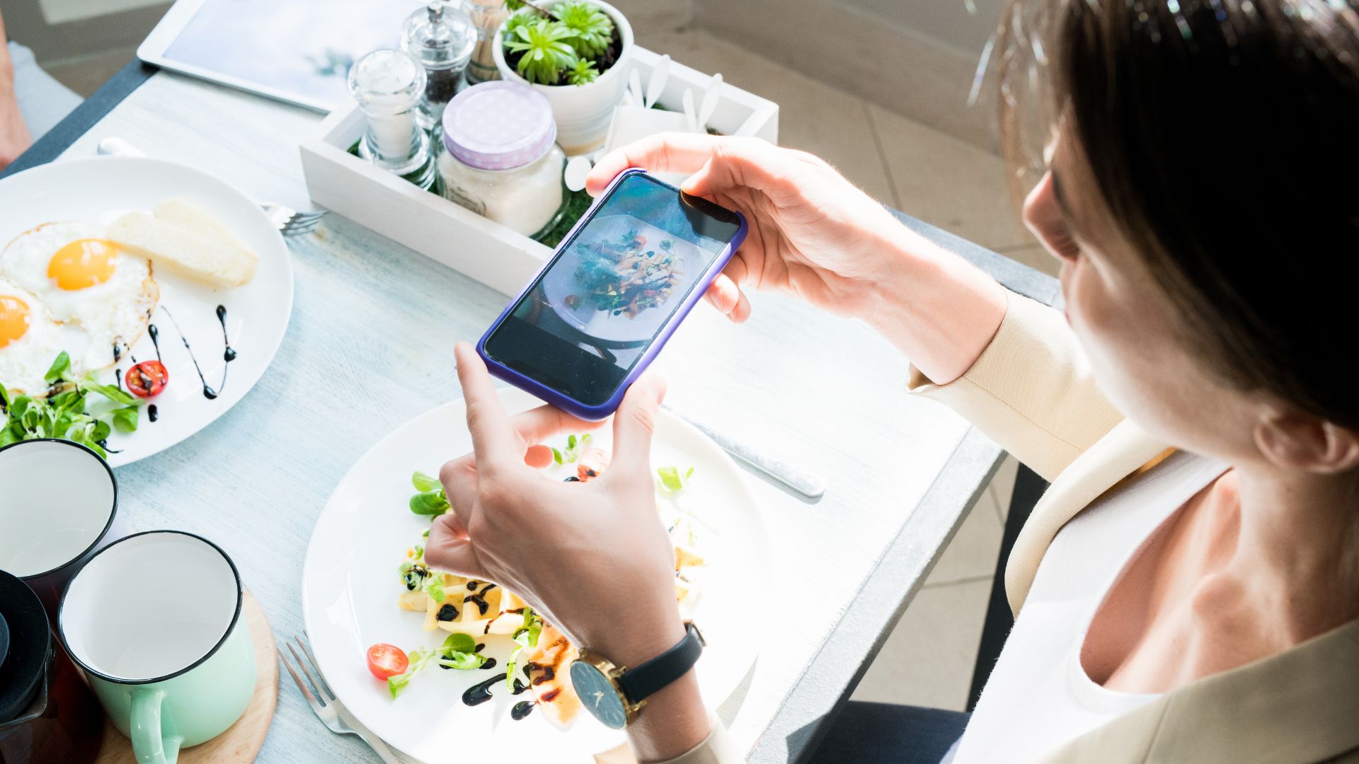 image showing a food critic at a table taking pictures of food in front of her on her phone