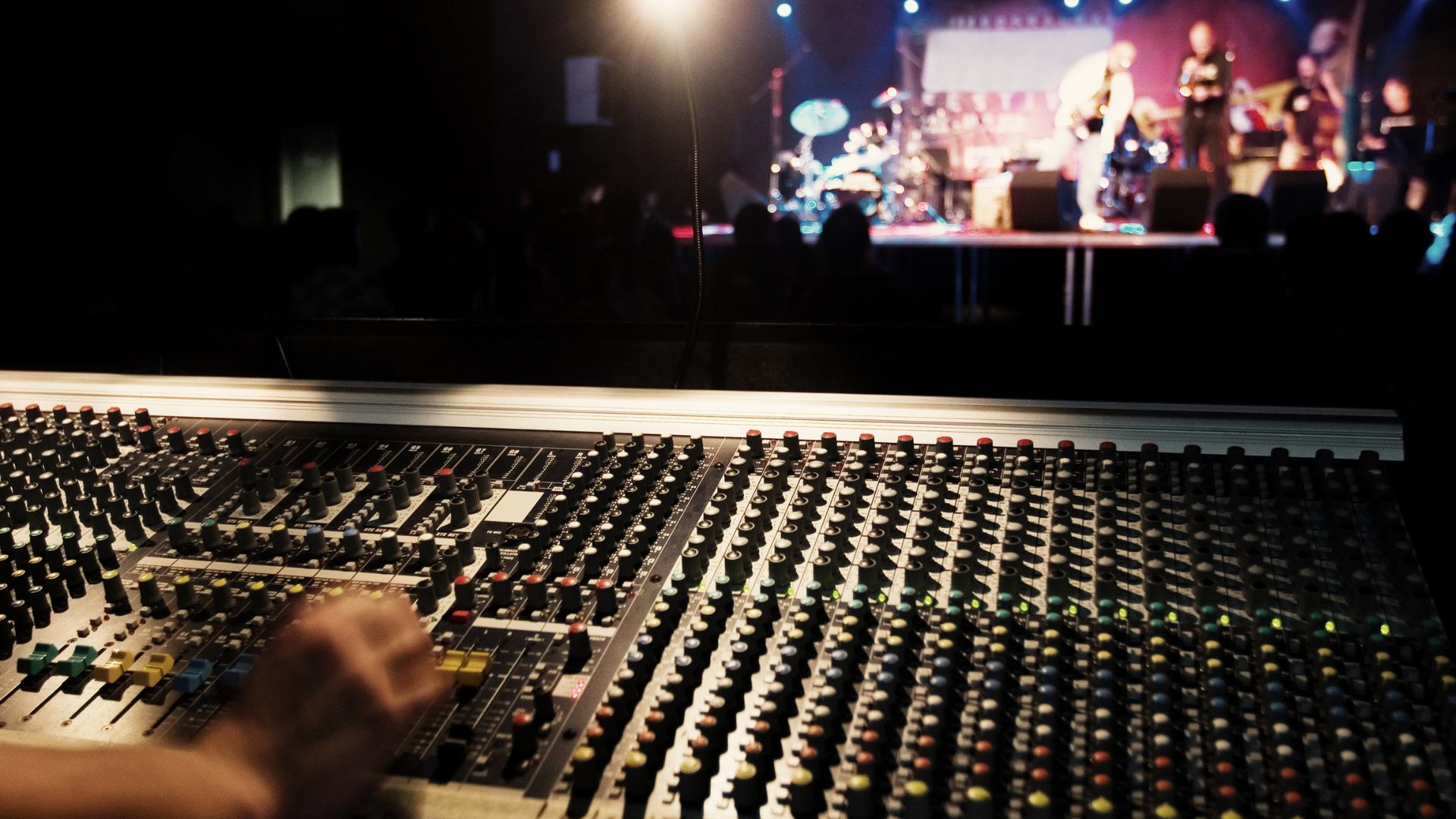 image showing a sound technician sitting in front of an audio control board in an auditorium